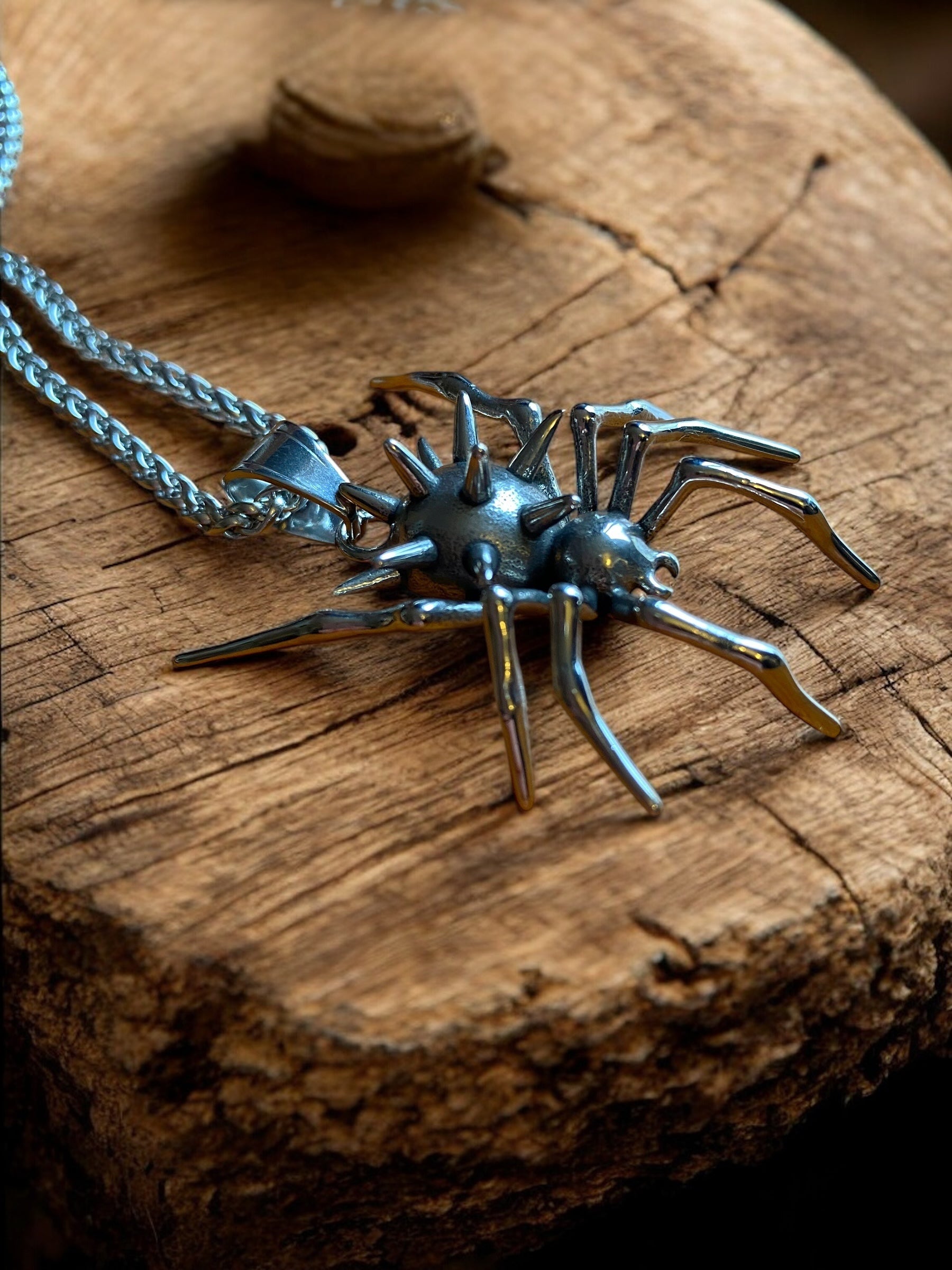 A steel necklace with a spider showing a spiked body and pincers.