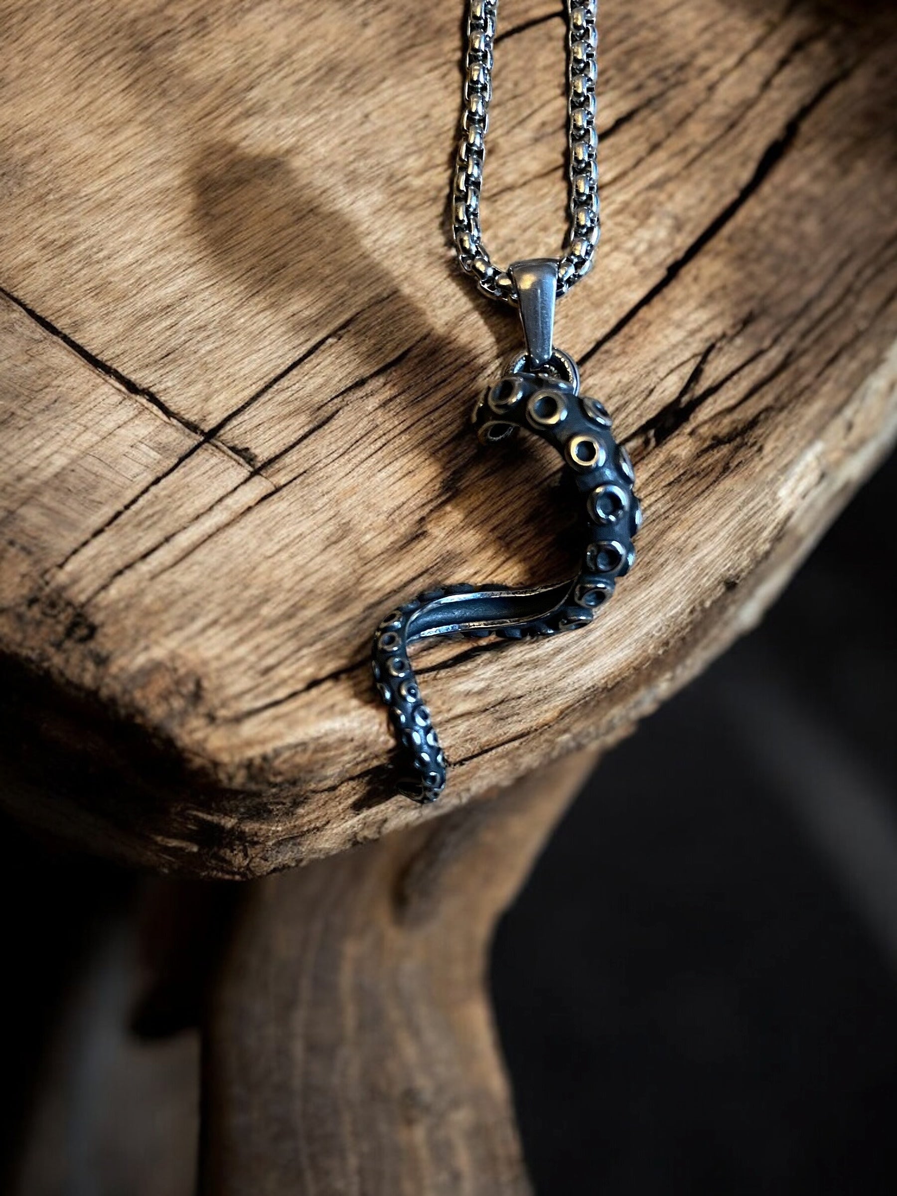 Close up of a viking necklace with an octopus tentacle-shaped pendant made of stainless steel, displayed on a wooden surface.