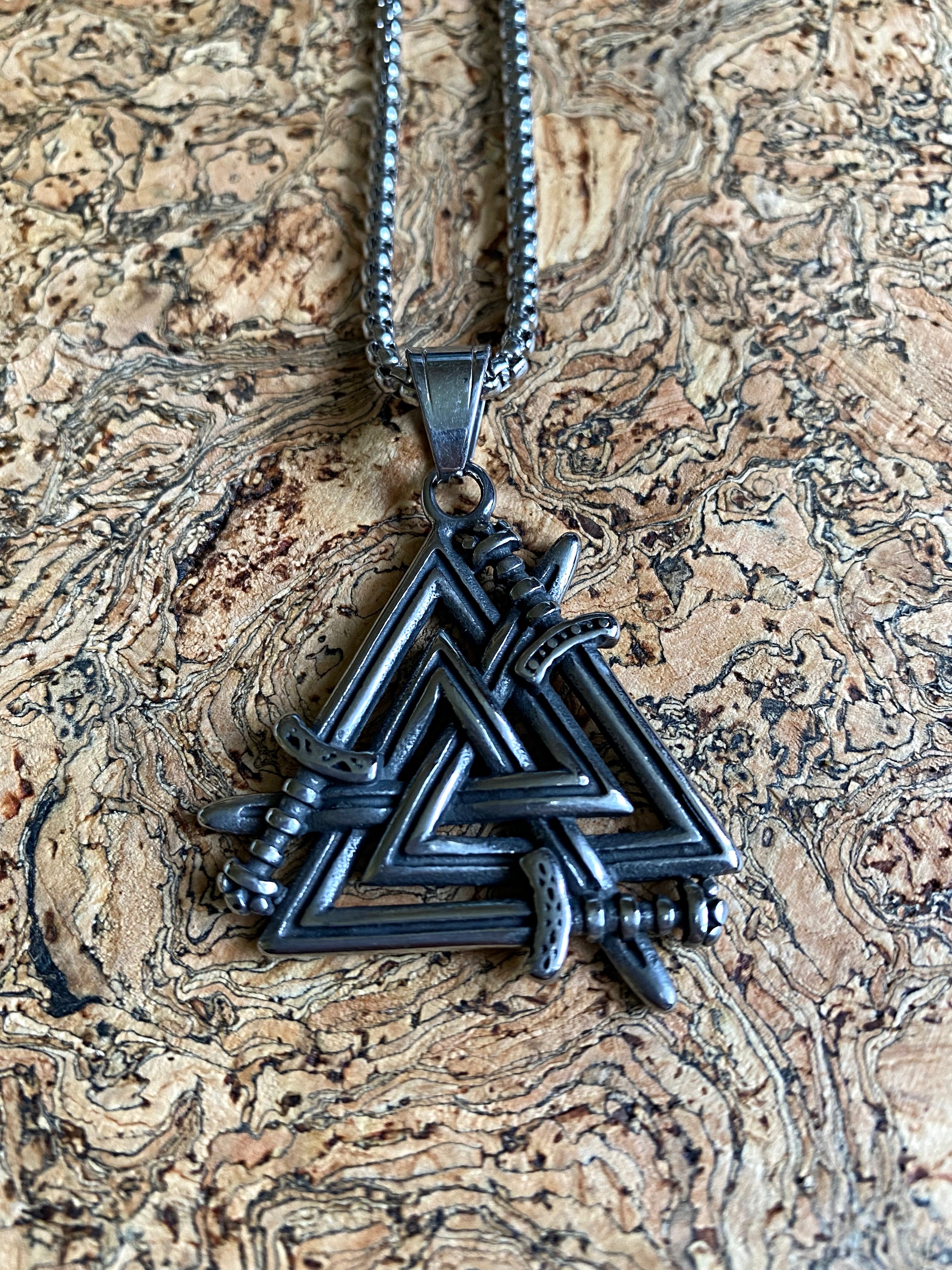 A stainless steel Valknut silver necklace placed on a textured background.