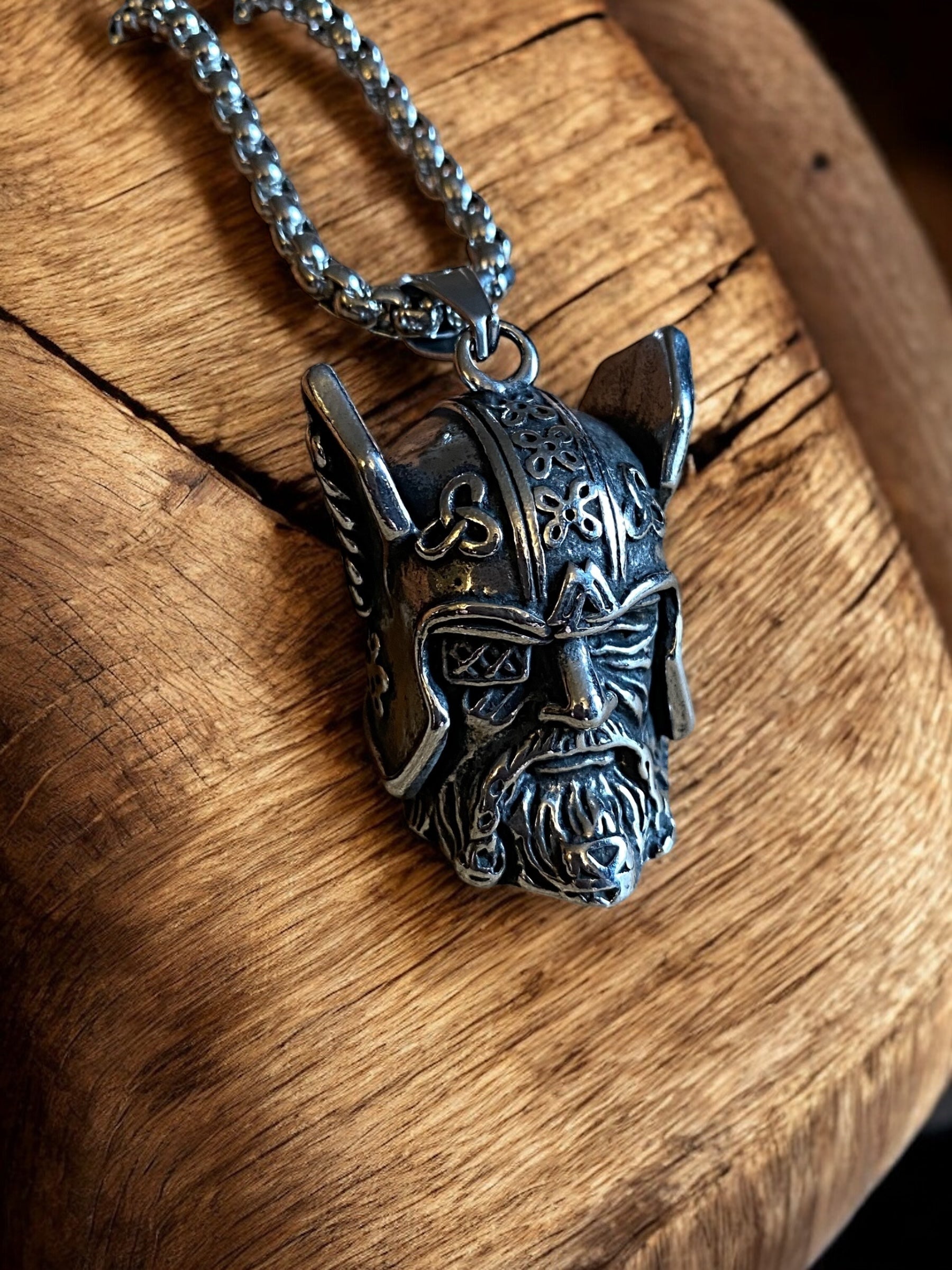 A 3D sterling silver necklace featuring a realistic Viking head with intricate detailing, displayed on a wooden surface.