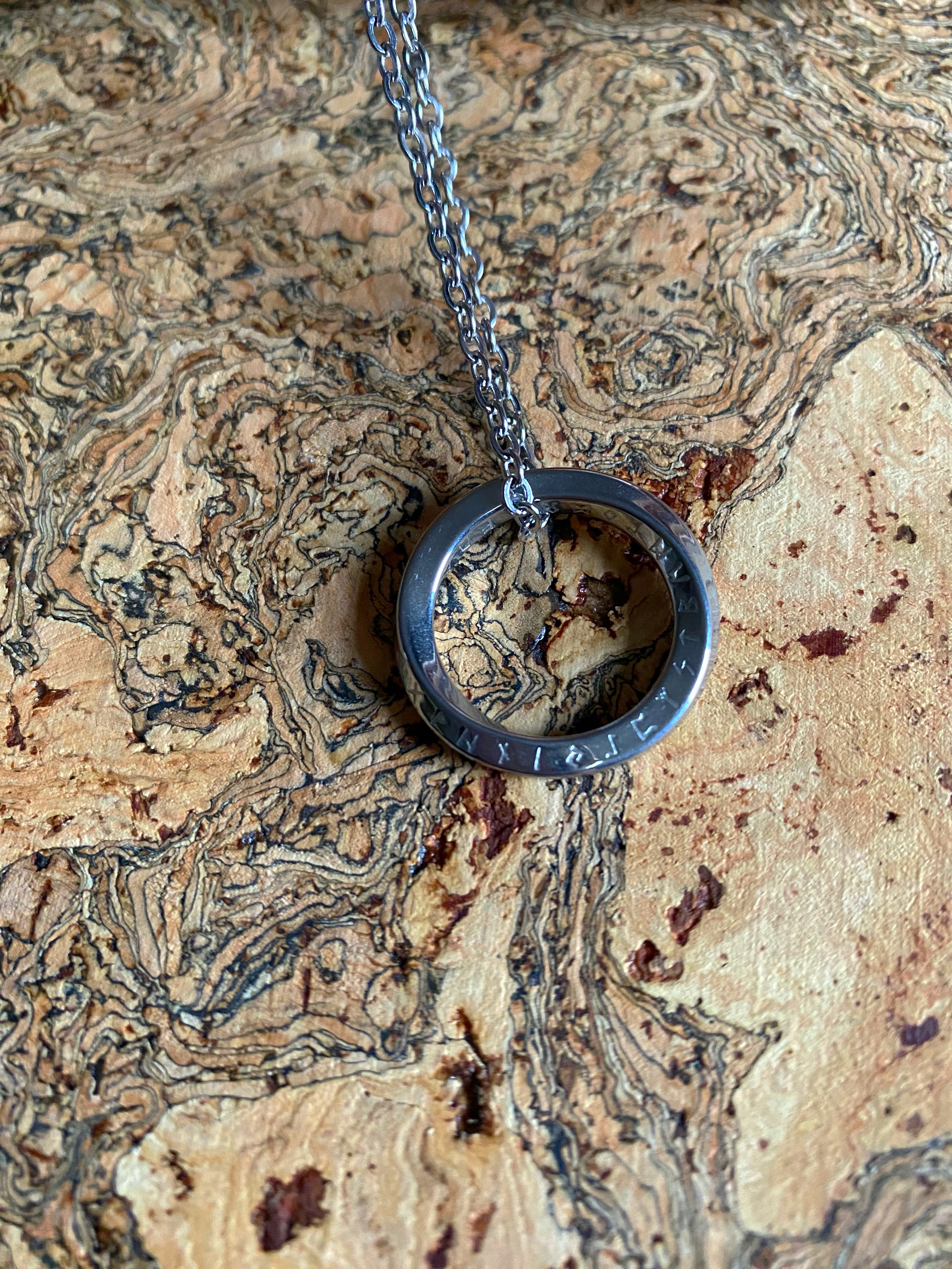 A Viking necklace with a runic sphere pendant on a chain, displayed on a textured background.