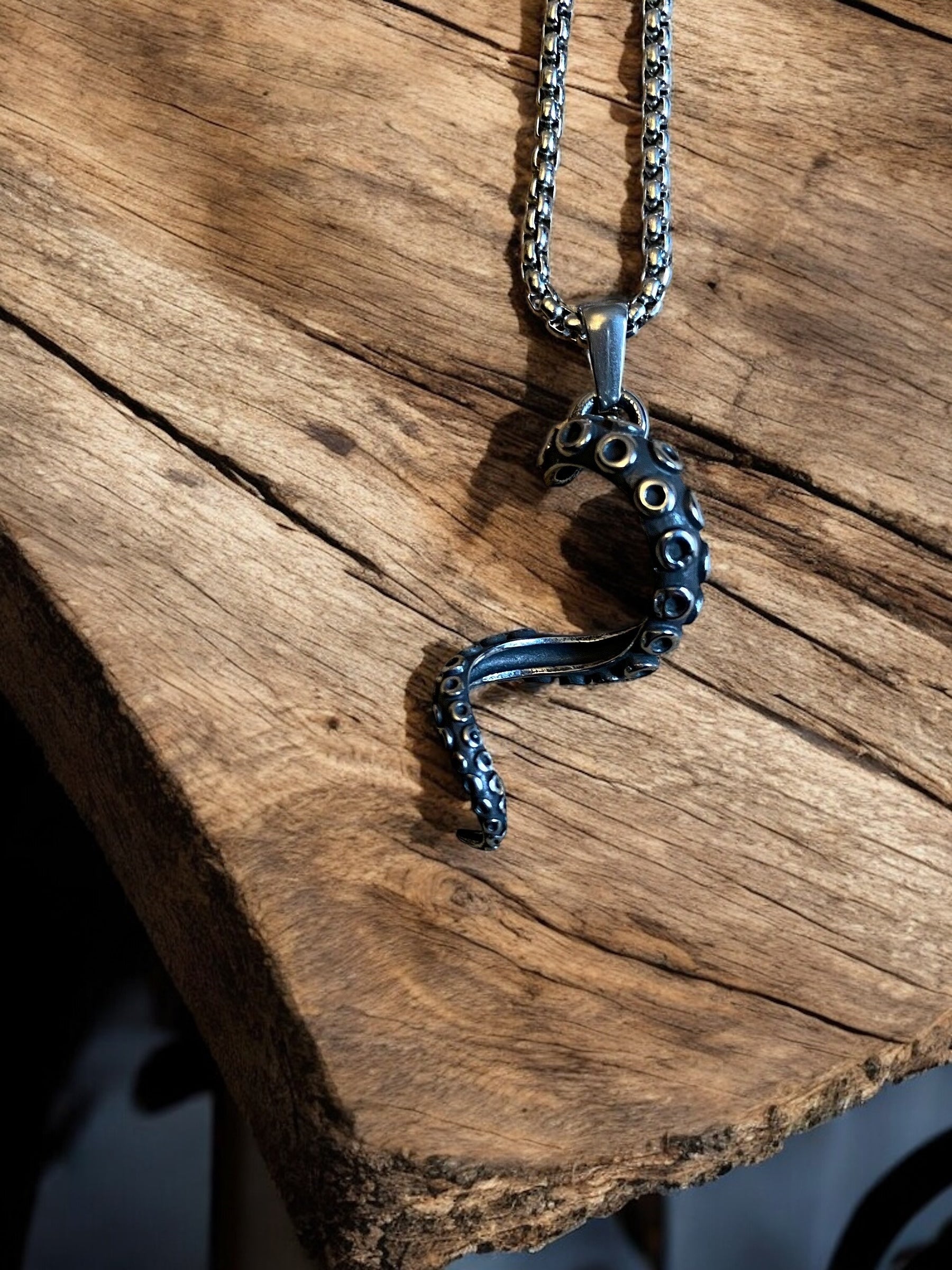 A viking necklace with an octopus tentacle-shaped pendant made of stainless steel, displayed on a wooden surface.