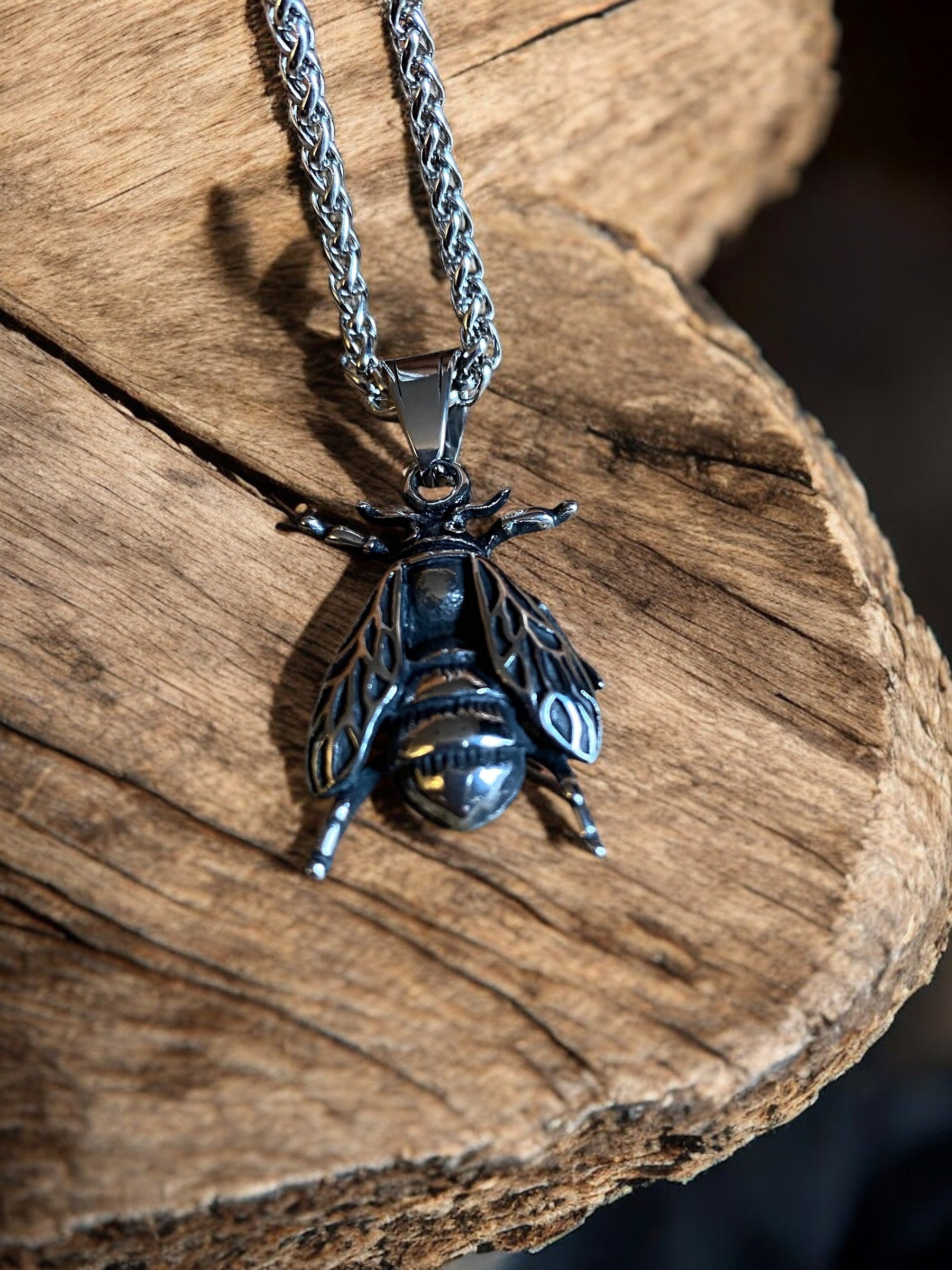 Front view of the fly pendant necklace on a wooden surface.
