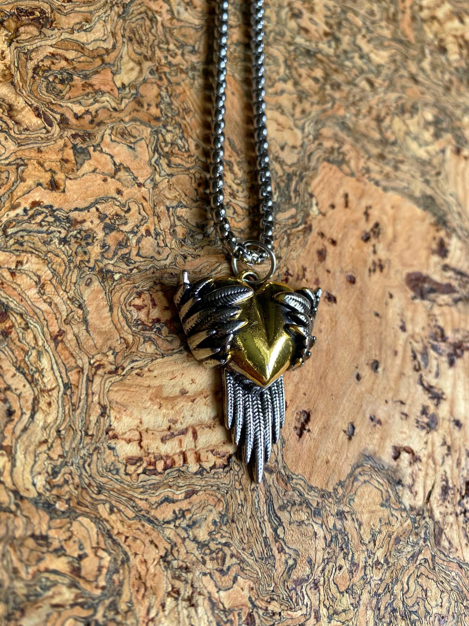 A Norse raven necklace featuring a stainless steel raven with a golden heart design on the pendant, displayed against a wooden background.