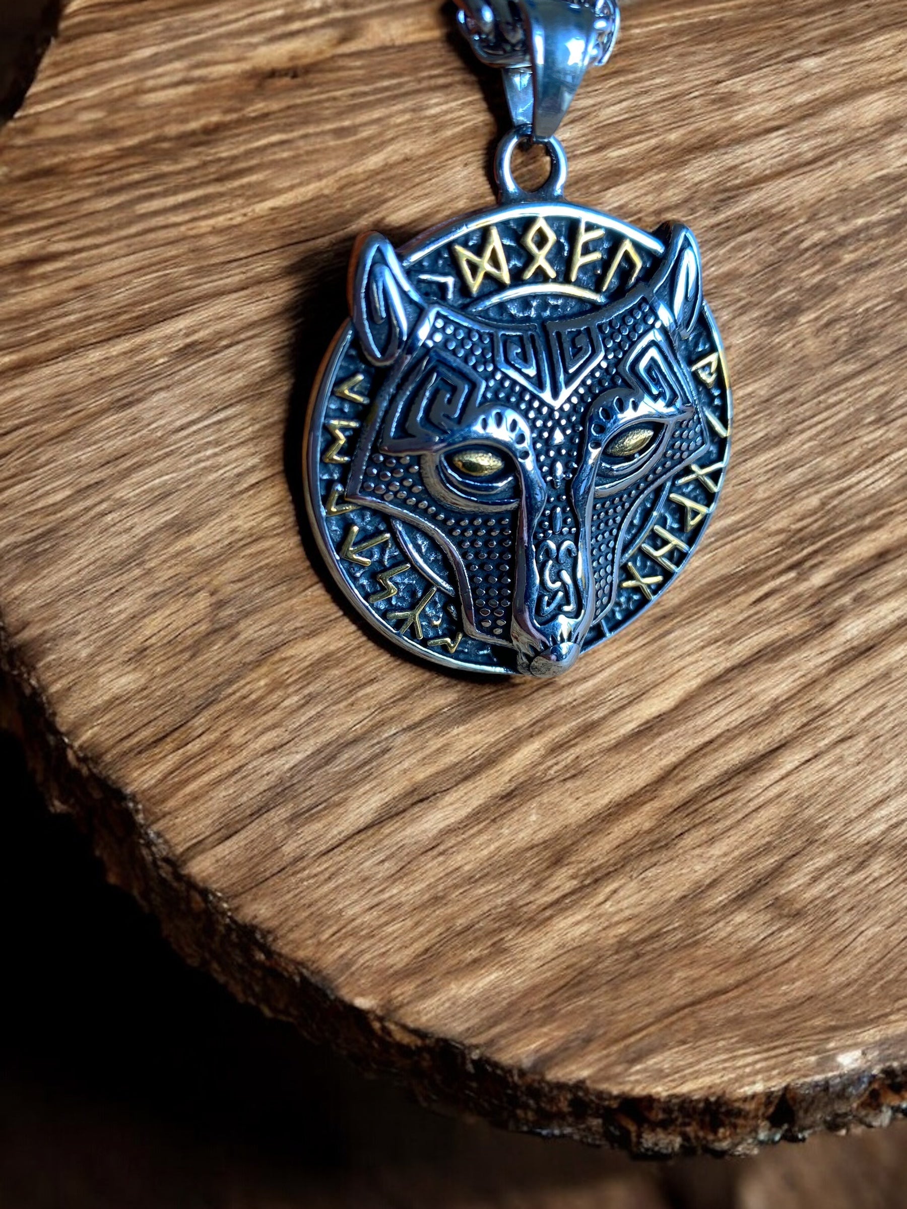 A stainless steel pendant necklace featuring a detailed depiction of the Fenrir Wolf head, with gold runes around its circumference.