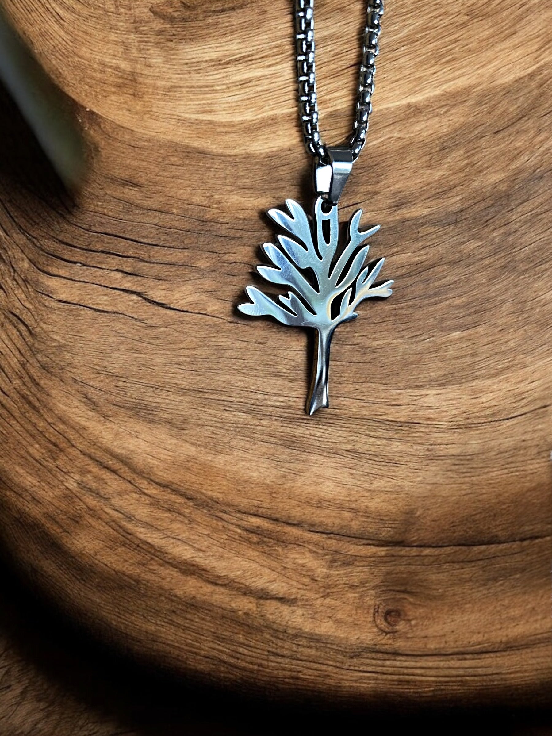 A silver-colored Yggdrasil Tree of Life necklace made of stainless steel, displayed against a wooden background.