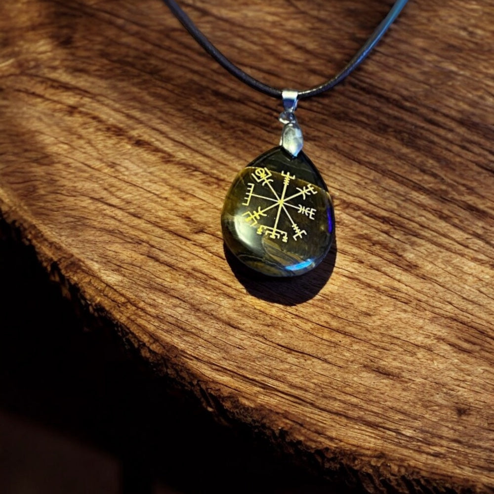 A pendant necklace with a pebble featuring the Aegishjalmur symbol on a black cord.